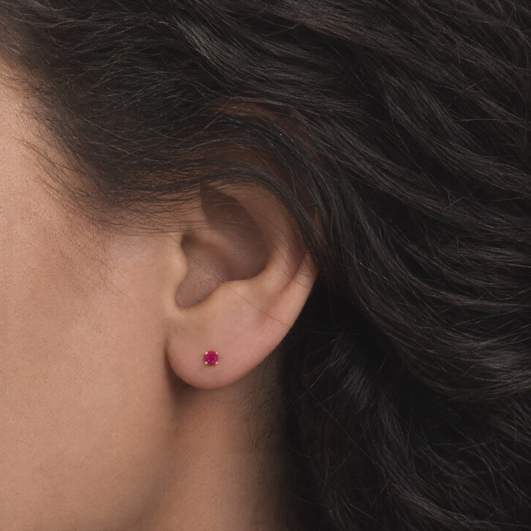 Broquel Solitario Zirconia Magenta 3 mm Oro 10K puesto en la oreja: la modelo se acomoda el cabello.