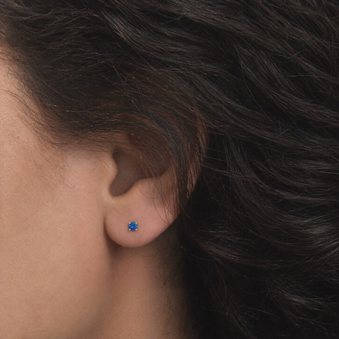 Broquel Solitario Zirconia Azul 3 mm Oro 10K puesto en la oreja: la modelo se acomoda el cabello.