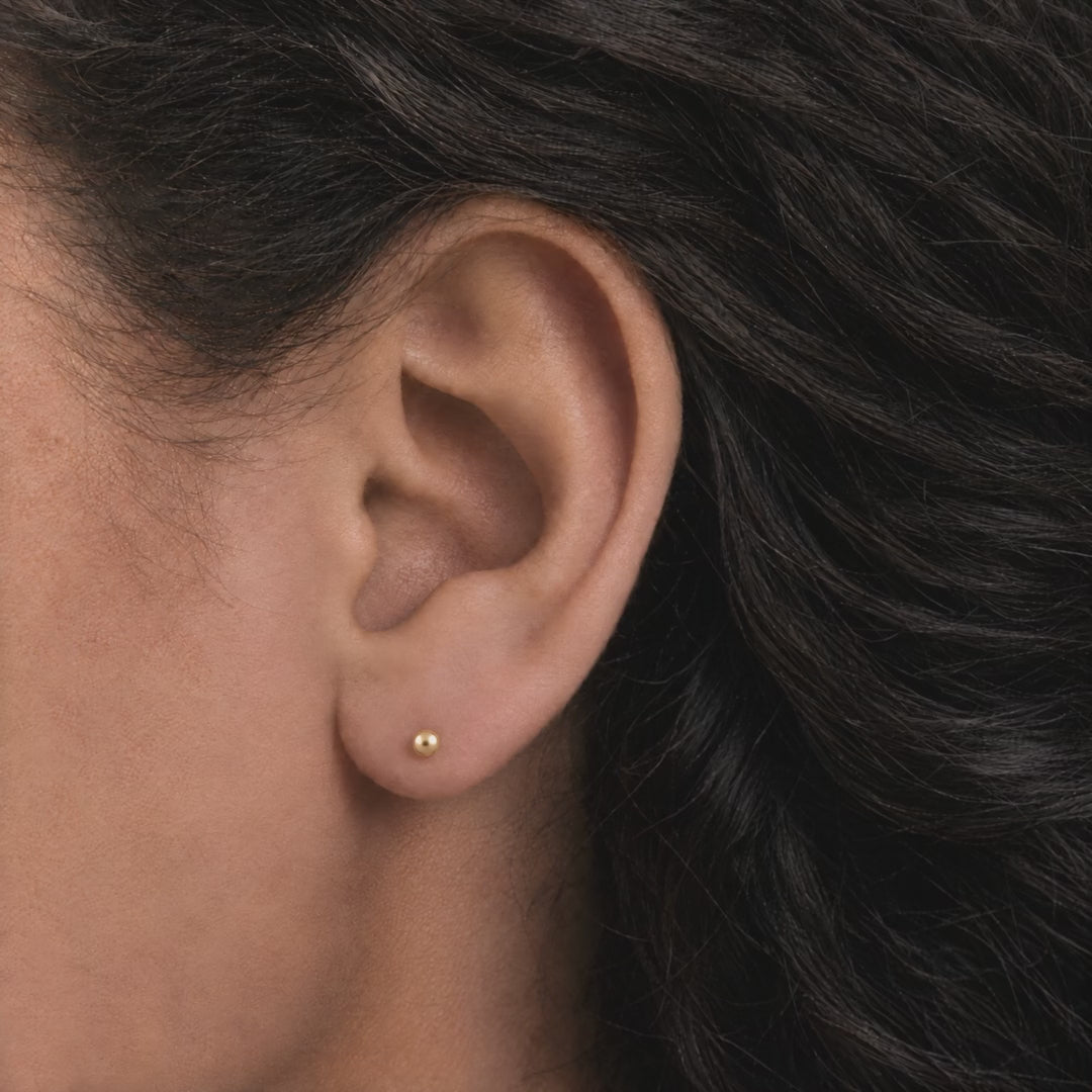 Broquel Dormilona 2.8 mm Oro 10K puesto en la oreja: la modelo se acomoda el cabello.