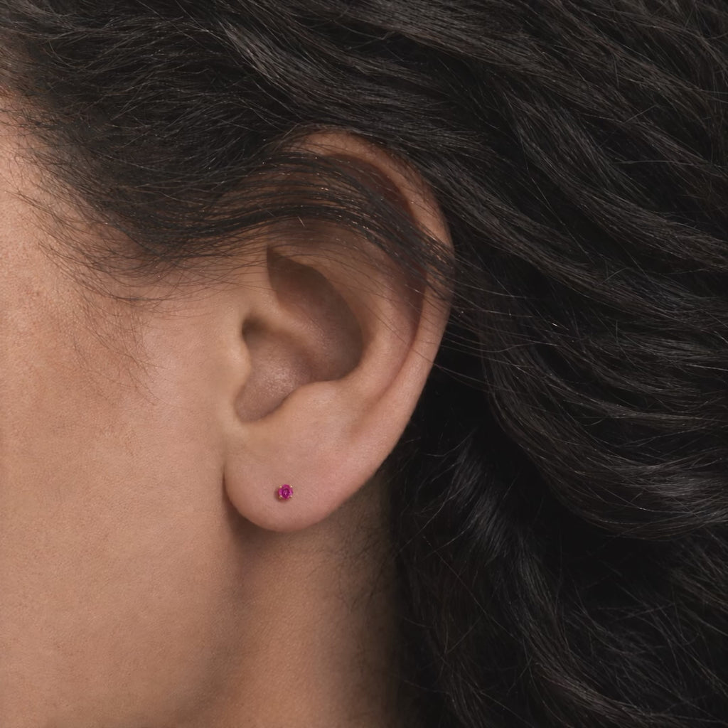 Broquel Solitario Zirconia Magenta 2.25 mm Oro 10K puesto en la oreja: la modelo se acomoda el cabello.