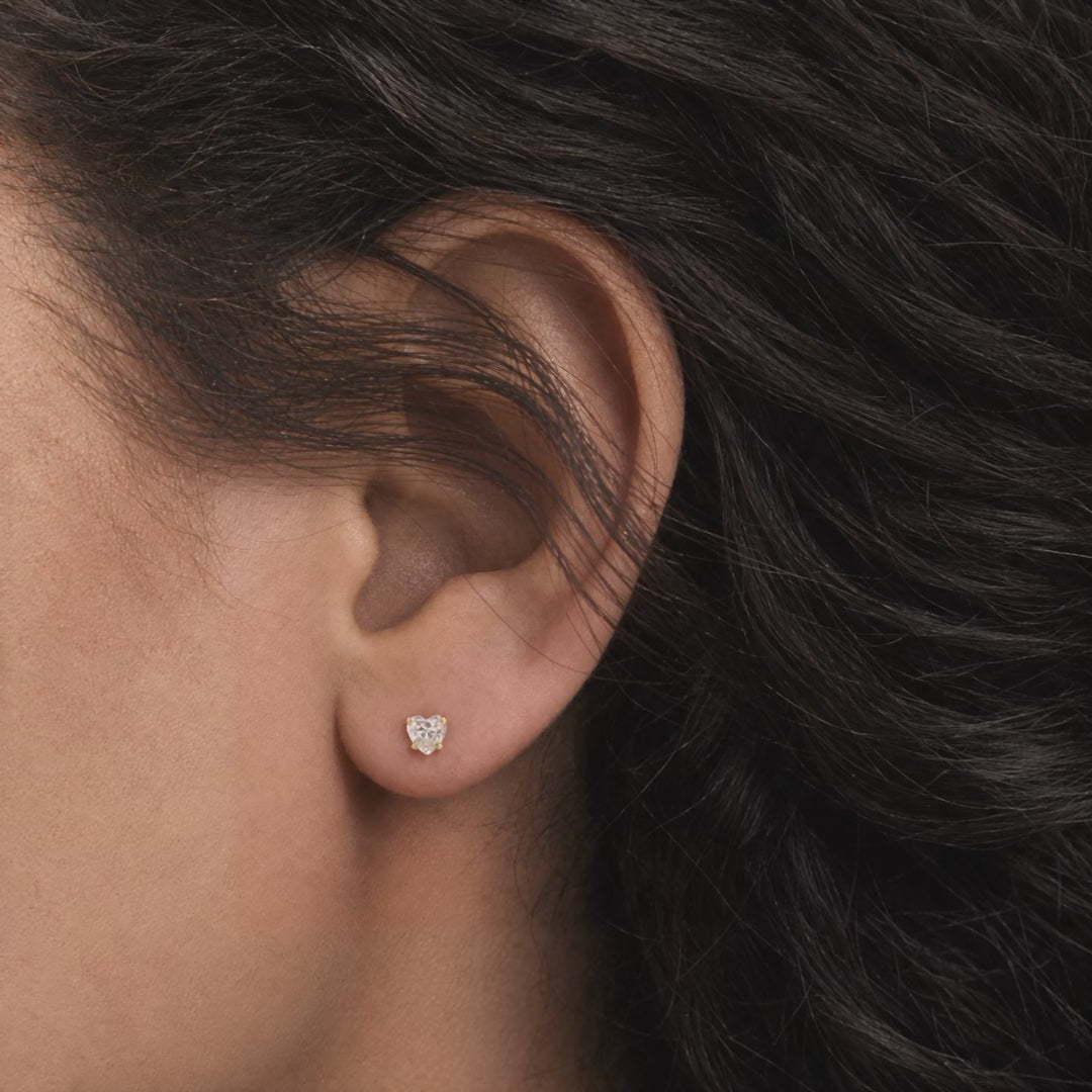 Broquel Corazón Zirconia 4 mm Oro 10K puesto en la oreja: la modelo se acomoda el cabello.