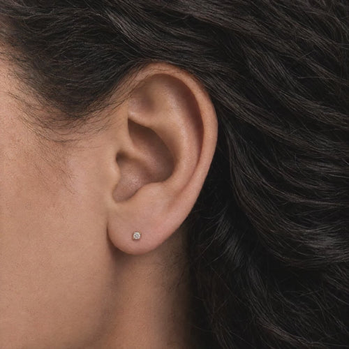 Broquel Solitario Zirconia Blanca 2.25 mm Oro 10K puesto en la oreja: la modelo se acomoda el cabello.