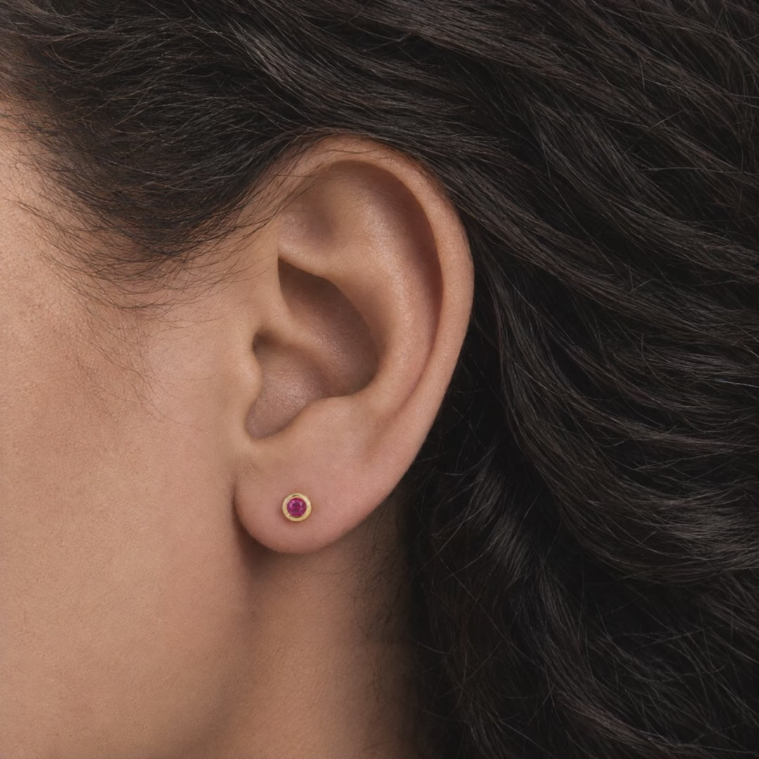 Broquel Bisel Zirconia Magenta 3 mm Oro 10K puesto en la oreja: la modelo se acomoda el cabello.