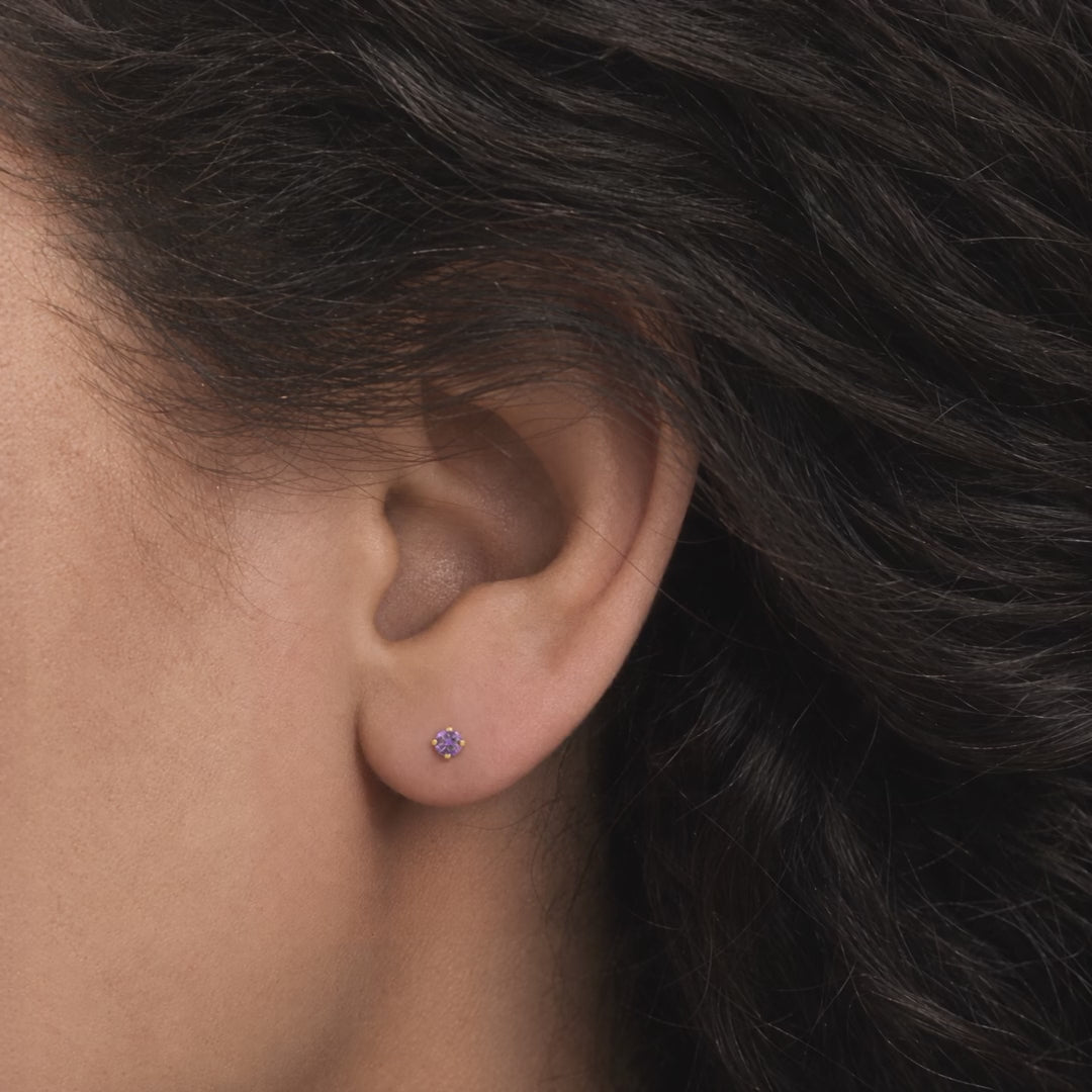 Broquel Solitario Zirconia Amatista 3 mm Oro 10K puesto en la oreja: la modelo se acomoda el cabello.