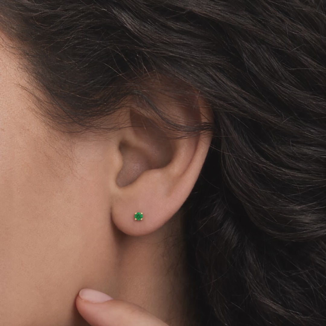 Broquel Solitario Zirconia Verde 3 mm Oro 10K puesto en la oreja: la modelo se acomoda el cabello.